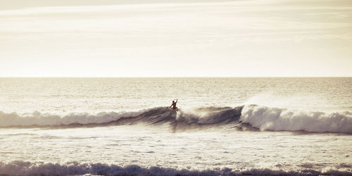 Silhouette teenage boy surfing in sea against sky during sunset