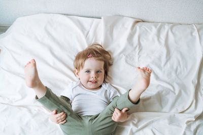 Cute funny baby girl angry child in home clothes on bed at home, view from top