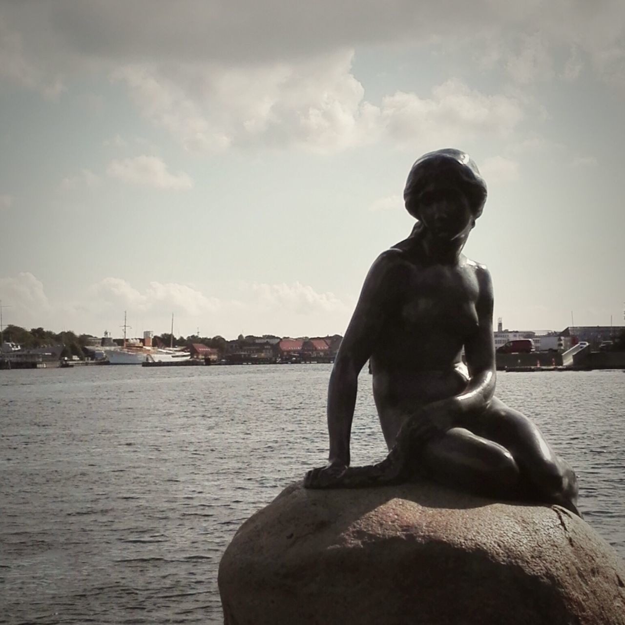 MAN SITTING BY STATUE AGAINST SEA