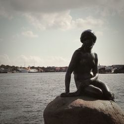 Man sitting by statue against sea against sky