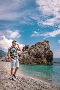 Man standing on rock by sea against sky