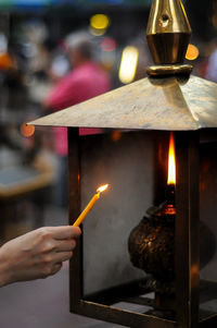 Close-up of hand lighting oil lamp with candle