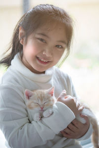 Portrait of smiling girl with sleeping scottish fold cat sitting by window at home