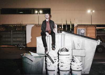 Full length portrait of young man sitting in illuminated factory