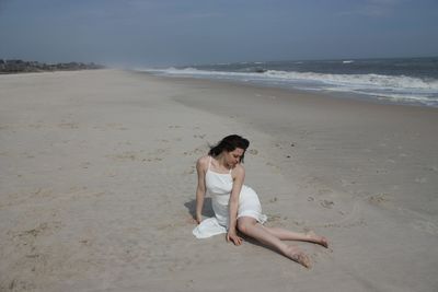 Woman sitting on beach against sky