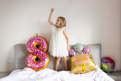 Full length of girl standing on bed by balloon