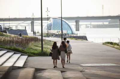 People walking on promenade along river in sunny day