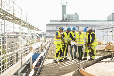 Architects and construction workers analyzing blueprint together at site