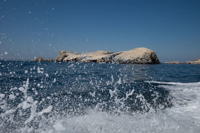 Sea waves splashing on rocks against clear sky