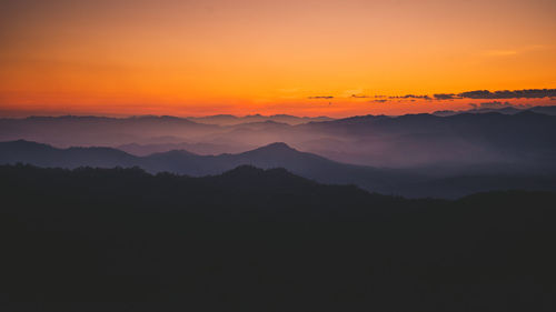 Scenic view of silhouette mountains against orange sky