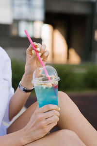 Blue non-alcoholic cocktail with a straw in a woman's hand close-up in summer