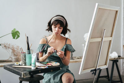 Woman sitting by easel against wall