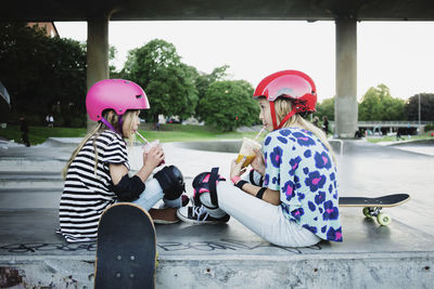 Friends drinking juice while sitting at skateboard park