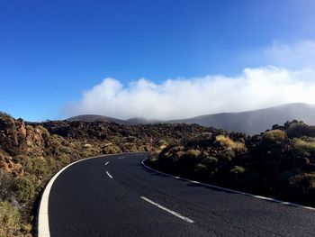 Road leading towards mountains against blue sky