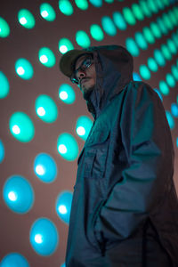 Close-up portrait of young man standing against illuminated wall