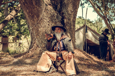 Portrait of man holding rifle while sitting in forest