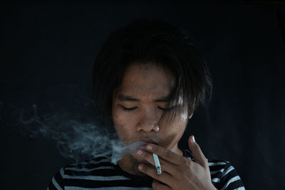 Close-up of woman smoking cigarette against black background