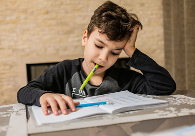 Cheerful and funny schoolboy solves  homework emotionally. thinks about how to solve math examples 