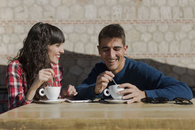 Smiling couple with coffee cups on table sitting at sidewalk cafe