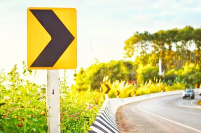 Arrow sign by road against sky