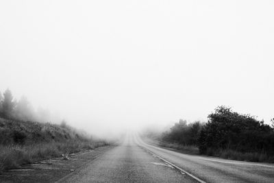 Empty road along trees against sky