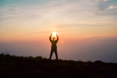 Optical illusion of person holding sun during sunset