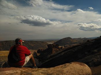 Rear view of man sitting on rock against sky