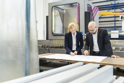 Businessman and businesswoman looking at plan on table in factory