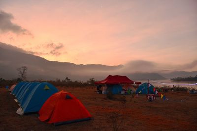 Tents at lakeshore against sky during sunset