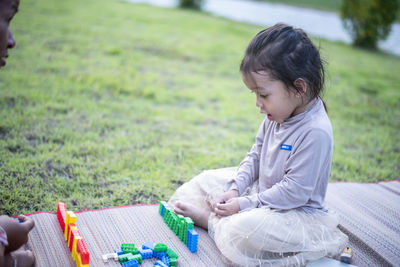 Side view of woman using mobile phone while sitting on field