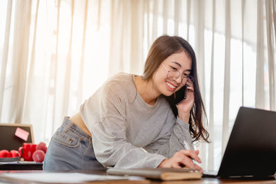 Smiling woman using laptop while talking on phone