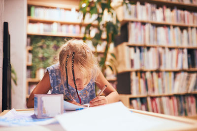 Schoolgirl doing homework. elementary student learning, drawing pictures in school library