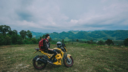 Man with motorcycle on field against sky