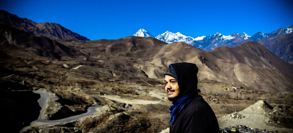 Man looking away while standing against mountains and sky