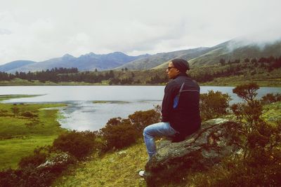 Lonely man sitting on a rock near lake