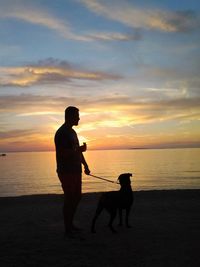 Silhouette of man and dog on beach during sunset