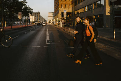 Female and male colleagues crossing street in city during sunset