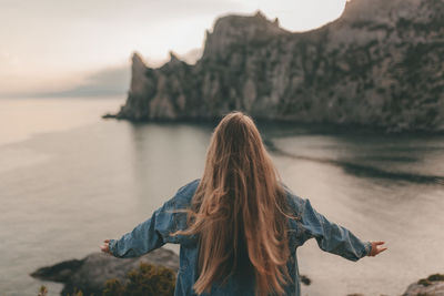 Young girl with long hair in a denim jacket against the backdrop of a mountain landscape