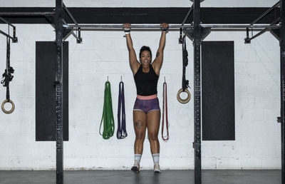 Woman working out on cross bars in a gym hanging from extended arms during a fitness workout.