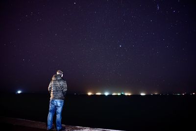Rear view of woman standing against illuminated star field at night