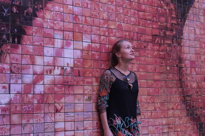 Full length of young woman standing against brick wall