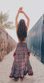 Rear view of woman with arms raised standing against sky