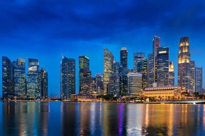 Illuminated modern buildings by bay against blue sky