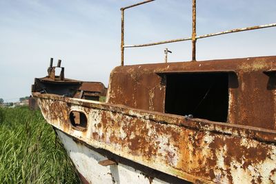 Abandoned boat on field against sky