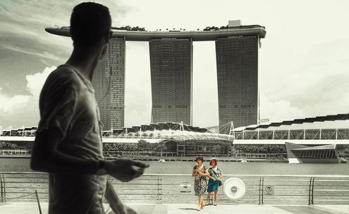 People on bridge in city against sky