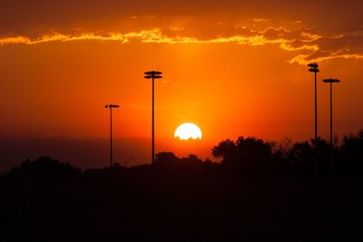 Silhouette trees and street lights against orange cloudy sky