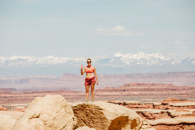 Female hiker in sports bra and shorts waves from a desert viewpoint