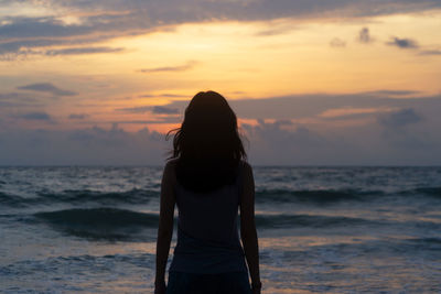 Rear view of woman standing at beach against sky during sunset