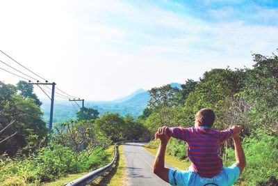 Rear view of father carrying son on shoulder against sky