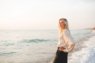 Elegant young woman wear stylish black pants and shirt standing in sea water over coast line outdoor